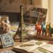 A collection of Travel Souvenir Ideas displayed on a wooden desk, including a miniature Eiffel Tower replica, a handwoven basket, a jar of seashells, traditional patterned tiles, colorful wooden toy animals, an open travel journal, and postcards.
