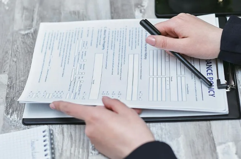 A person reviewing and filling out an insurance policy form with a pen, in the context of the blog titled 'What Not True About DoD Travel Policy.'"