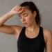 A young woman sweating after an intense workout, sitting on the gym floor and wiping her face with a towel.