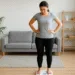 A young woman standing on a home weighing scale, checking her weight in a bright, minimalistic room.