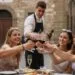 A group of five young adults (all over the legal drinking age of 18 in Italy), toast with wine glasses at an outdoor Italian cafe.