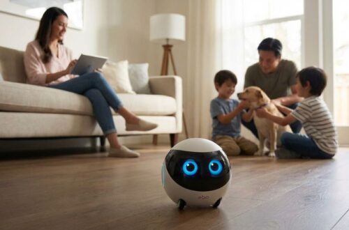A small, spherical Ebo robot with glowing blue digital eyes sitting on a wooden floor in a sunlit living room, with a family and a dog interacting in the background.