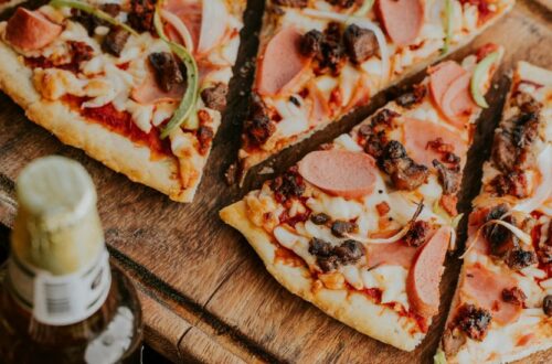 Slices of delicious Brooklyn Style Pizza topped with pepperoni, ham, sausage, and peppers on a rustic wooden board.