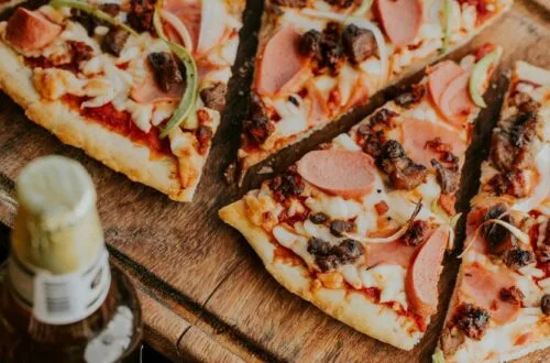 Slices of delicious Brooklyn Style Pizza topped with pepperoni, ham, sausage, and peppers on a rustic wooden board.