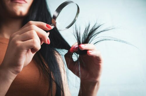 A close-up of a person using a magnifying glass to examine frayed split ends, showing exactly what Damaged Hair looks like under inspection.