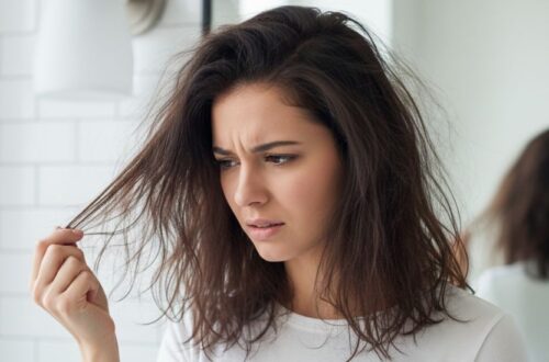 A concerned young woman looking at her dry, frizzy strands in a mirror to understand how to know if your hair is damaged.