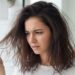 A concerned young woman looking at her dry, frizzy strands in a mirror to understand how to know if your hair is damaged.