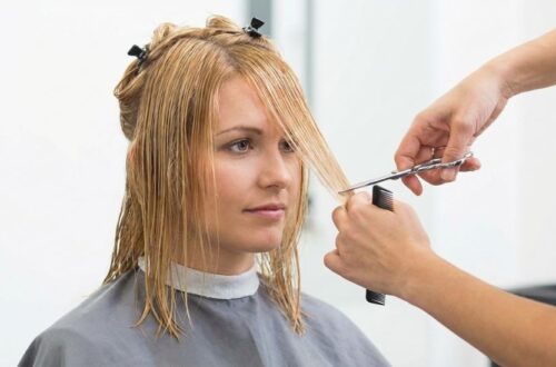 A woman with blonde hair having her face-framing layers trimmed in a professional salon setting, illustrating how to style a butterfly haircut for maximum volume.