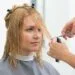 A woman with blonde hair having her face-framing layers trimmed in a professional salon setting, illustrating how to style a butterfly haircut for maximum volume.