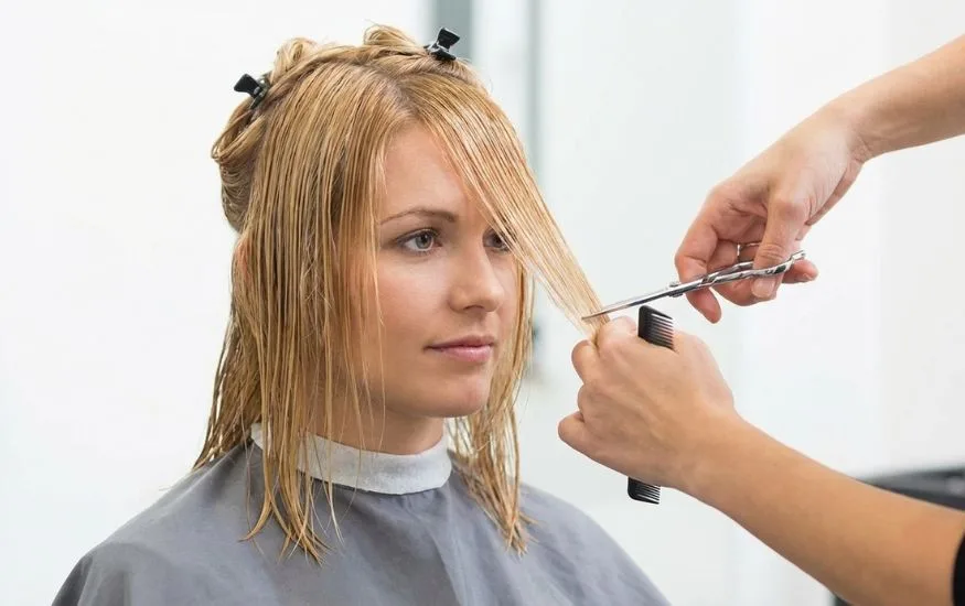 A woman with blonde hair having her face-framing layers trimmed in a professional salon setting, illustrating how to style a butterfly haircut for maximum volume.