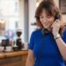 A young woman with a brown wolf cut hairstyle smiling while talking on a vintage black rotary phone in a cozy cafe setting. How to style a wolf cut to look effortless and voluminous.
