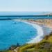 A scenic aerial view of a sunny coast showcasing popular things to do in Newport Beach, with beachgoers enjoying the clear ocean waters, sandy shore, and grassy overlook.