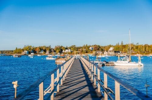 Things to Do in Rockland, Maine - Wooden pier extending into the blue water of Rockland Harbor with docked boats and coastal town buildings in the background.