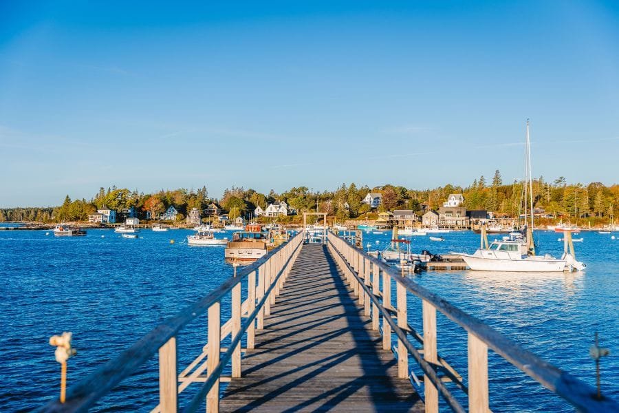 Things to Do in Rockland, Maine - Wooden pier extending into the blue water of Rockland Harbor with docked boats and coastal town buildings in the background.