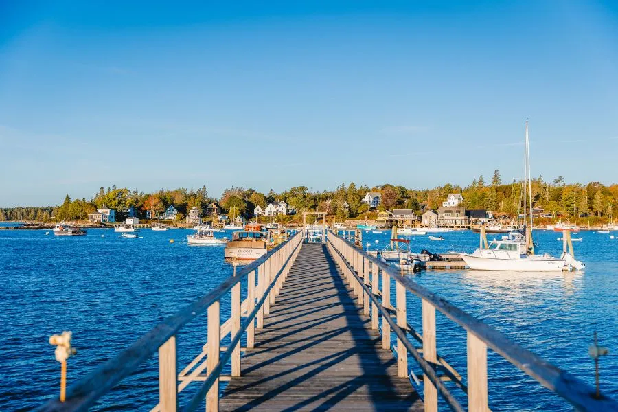 Things to Do in Rockland, Maine - Wooden pier extending into the blue water of Rockland Harbor with docked boats and coastal town buildings in the background.