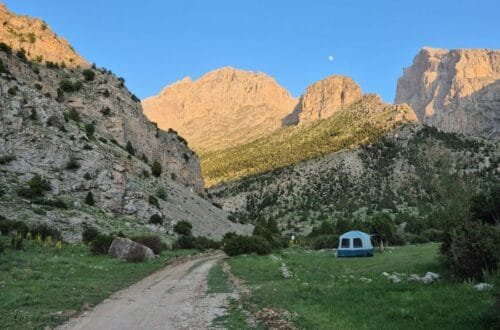 Guadalupe Mountains National Park landscape with rugged rocky peaks, green vegetation, a dirt trail, and a camping tent beneath a clear blue sky.